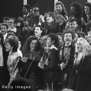 Stars sing "We Are The World," a song written to benefit famine victims in Ethiopia. Across the front row stands: Stevie Wonder, Lionel Richie, Sheila E., Diana Ross, Elizabeth Taylor, Michael Jackson, Smokey Robinson, Kim Carnes, Michael Douglas, and Janet Jackson.