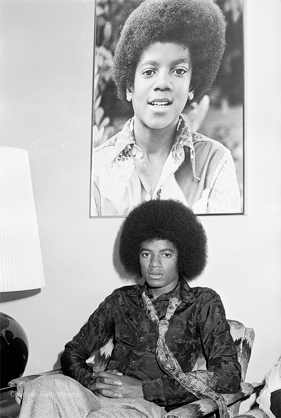 Michael Jackson poses beneath a photograph of his younger self in the 1970s.